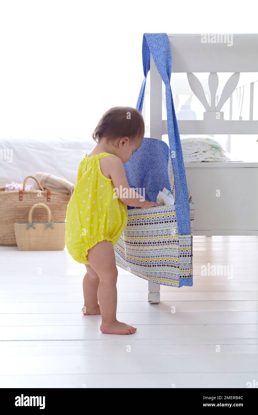 Bambina che guarda in borsa pannolino appeso dal retro della sedia, 13 mesi Foto Stock