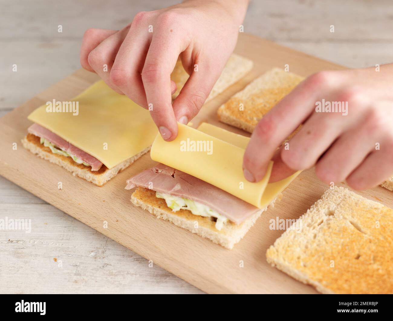 Club sandwich, aggiungendo fette di prosciutto e formaggio su fette tostate di pane bianco Foto Stock