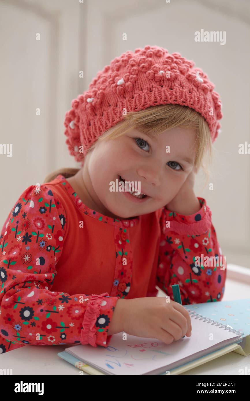 Ragazza che indossa berretto lavorato a maglia disegno foto in notebook, 3,5 anni Foto Stock