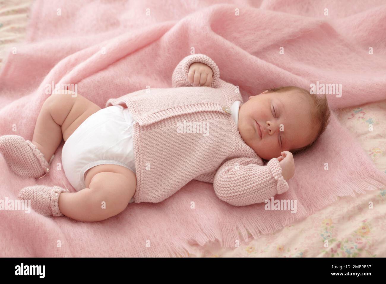 Bambina sdraiata con cardigan rosa lavorato a maglia e stivaletti, 6 settimane Foto Stock