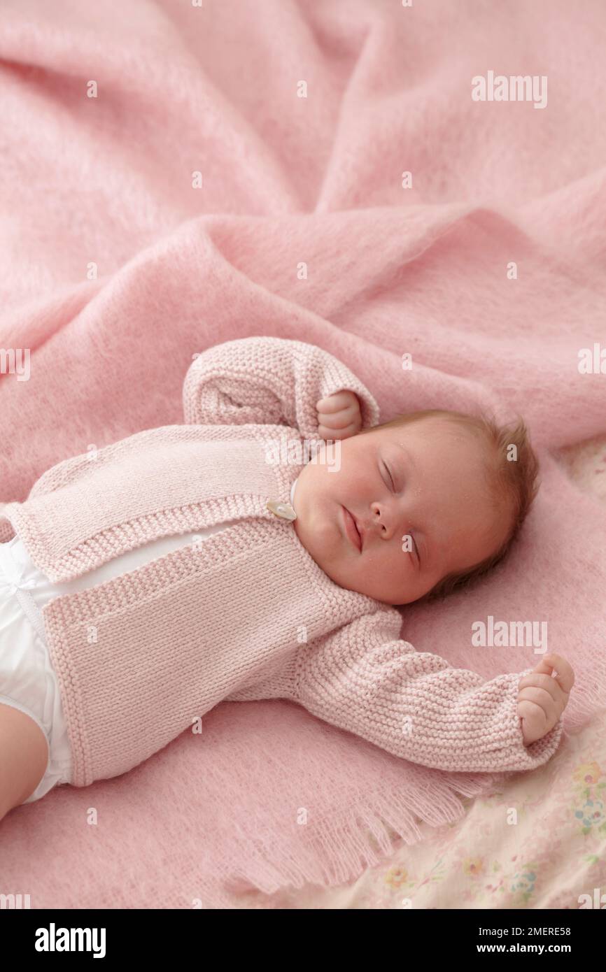 Bambina sdraiata con cardigan a maglia rosa, 6 settimane Foto Stock