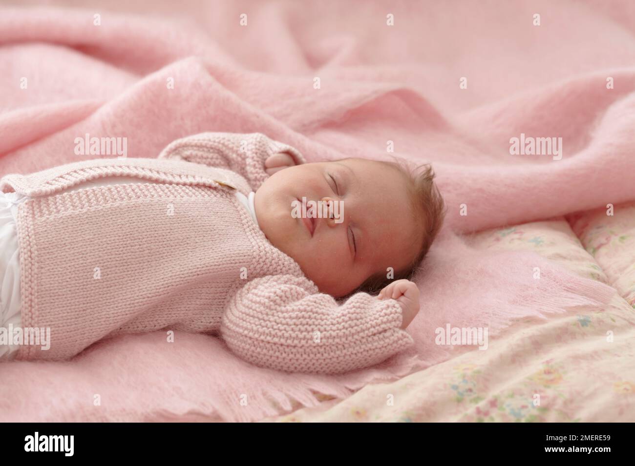 Bambina sdraiata con cardigan a maglia rosa, 6 settimane Foto Stock