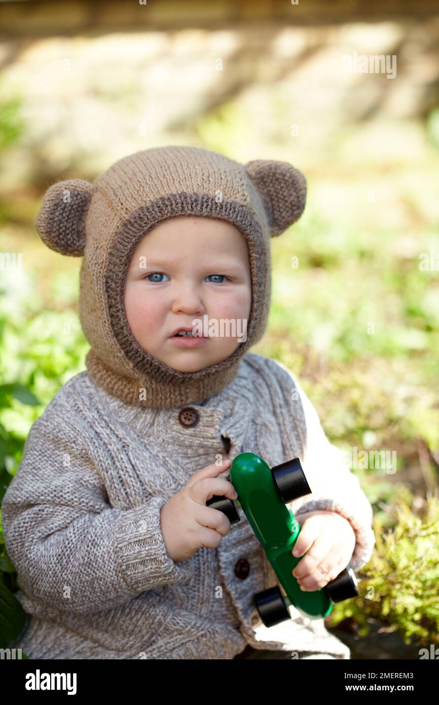 Ragazzo che indossa bearaclava e cardigan lavorato a maglia e che tiene l'auto giocattolo, 17 mesi Foto Stock