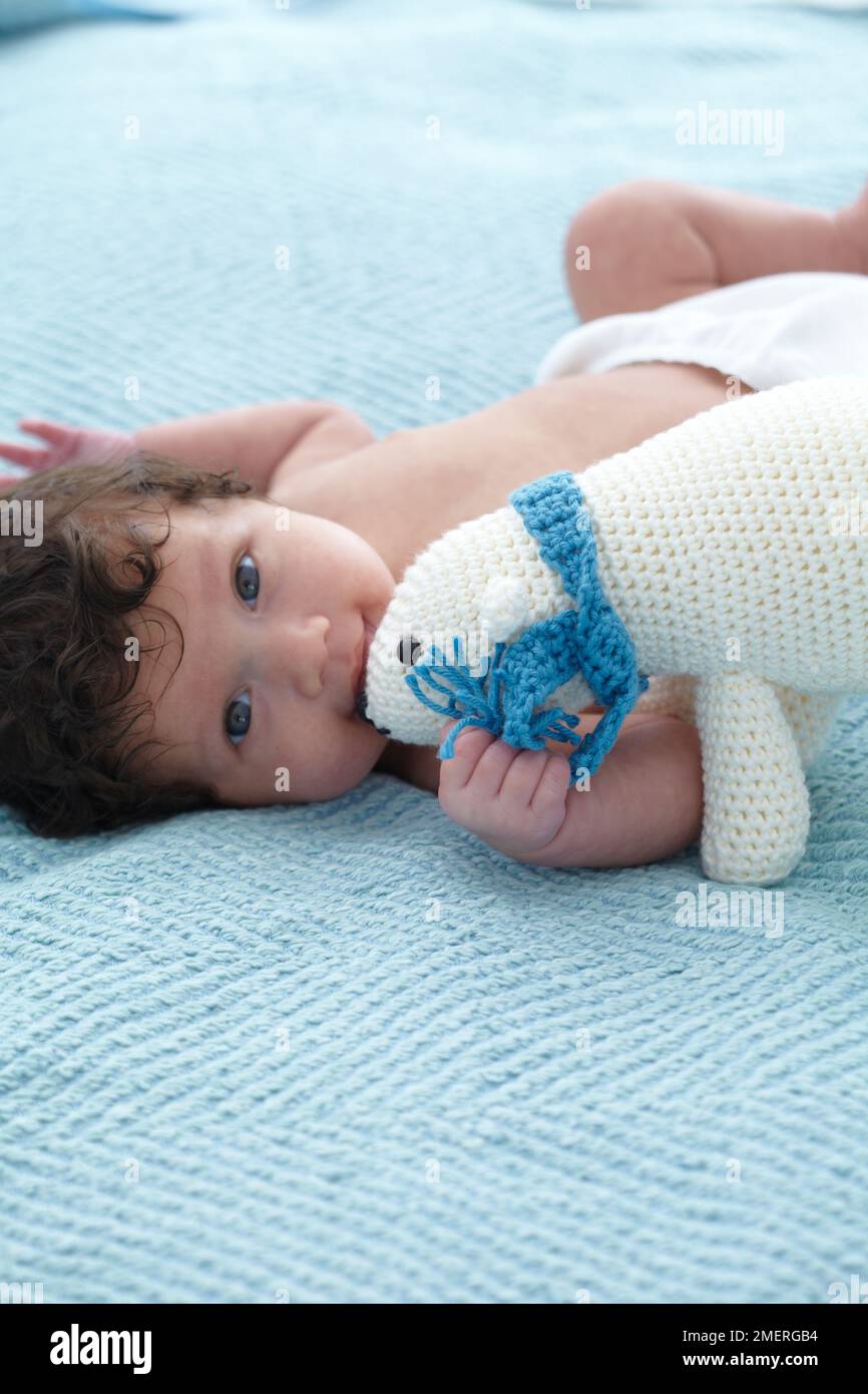 Bambino sdraiato sul letto guardando tenere un orso polare uncinetto, 4,5 mesi Foto Stock