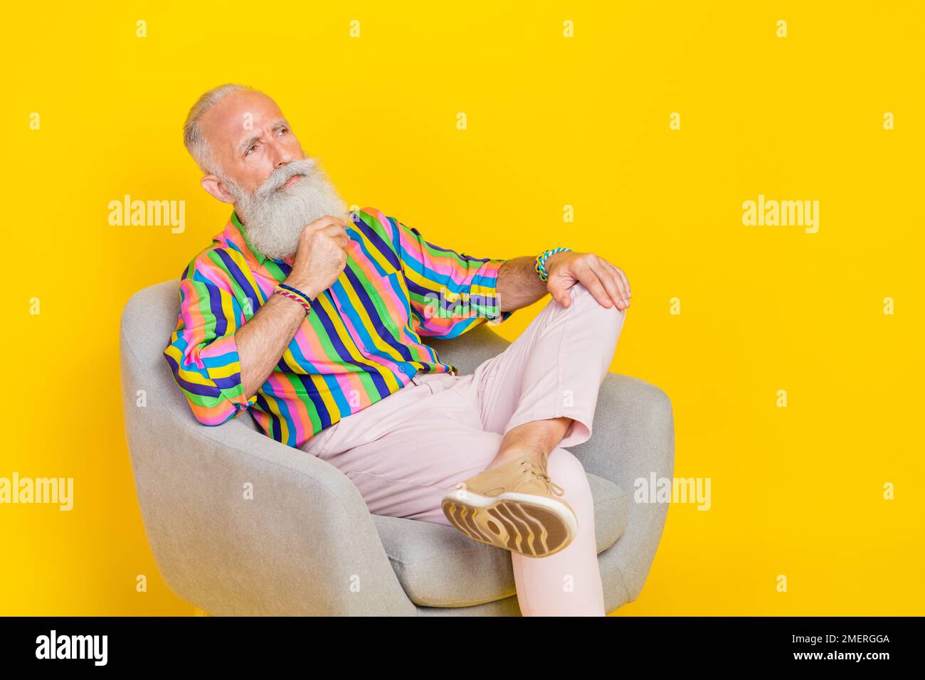 Foto di mentalità uomo anziano seduto poltrona braccio toccare barba guardare vuoto spazio ponder contemplare isolato su sfondo giallo Foto Stock