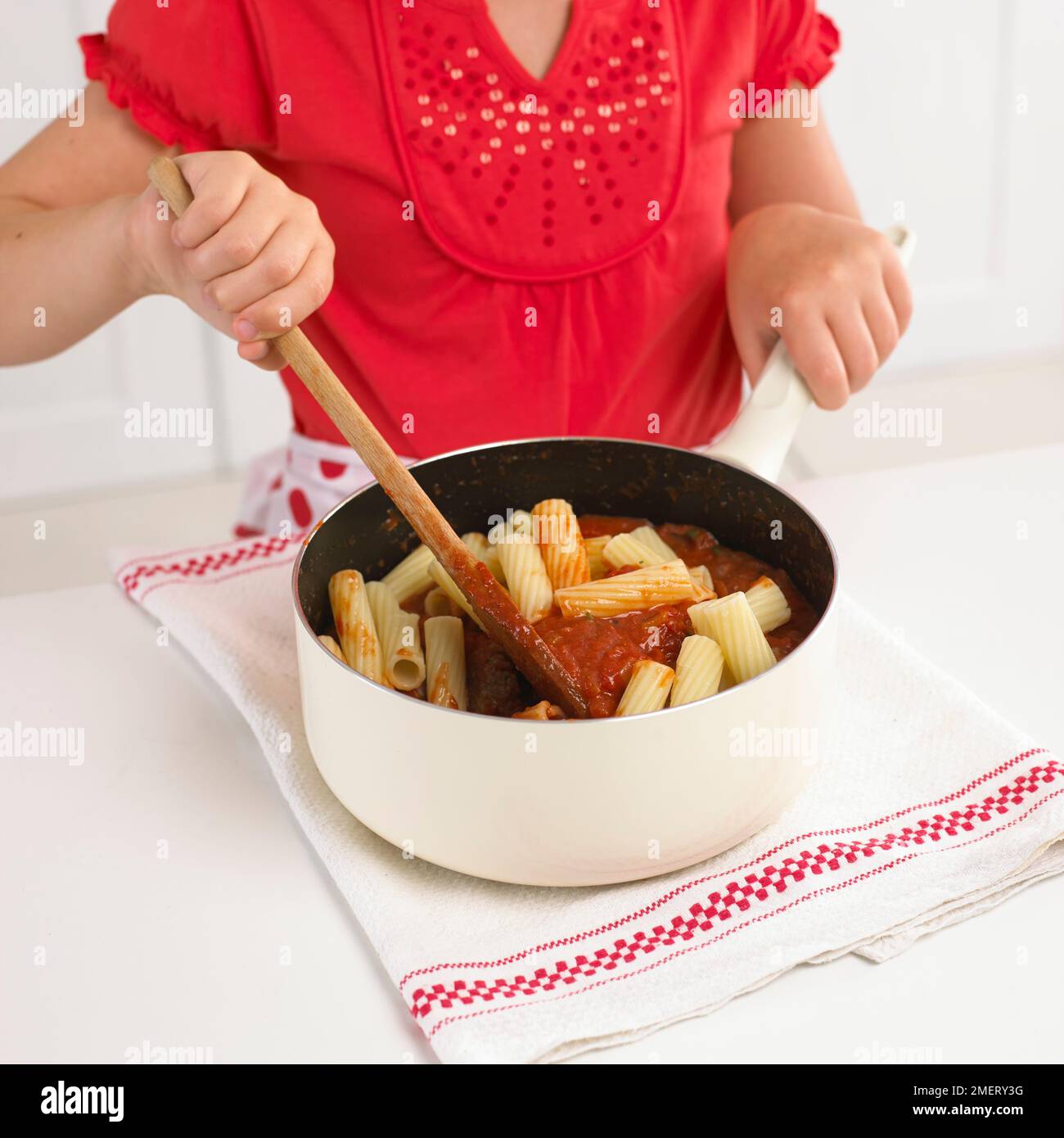 Ragazza che mescola la pasta in salsa di pomodoro Foto Stock