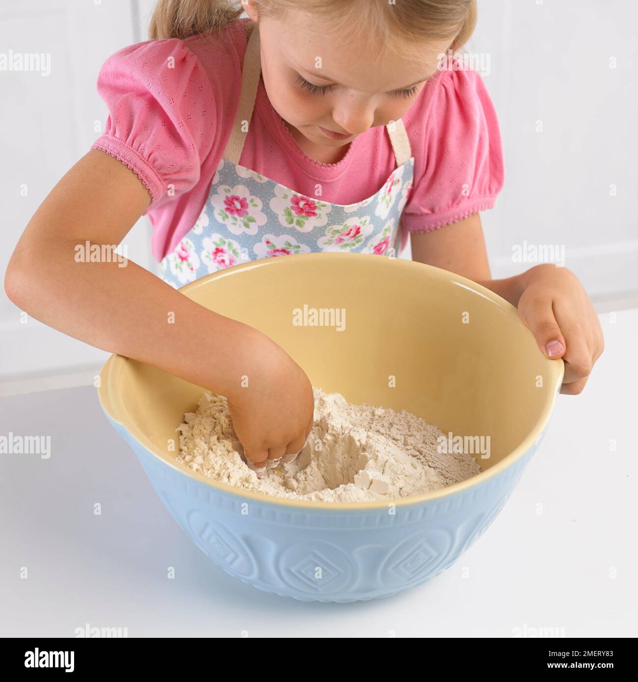Ragazza fare un pozzo in una ciotola di farina con la mano, 5 anni Foto Stock
