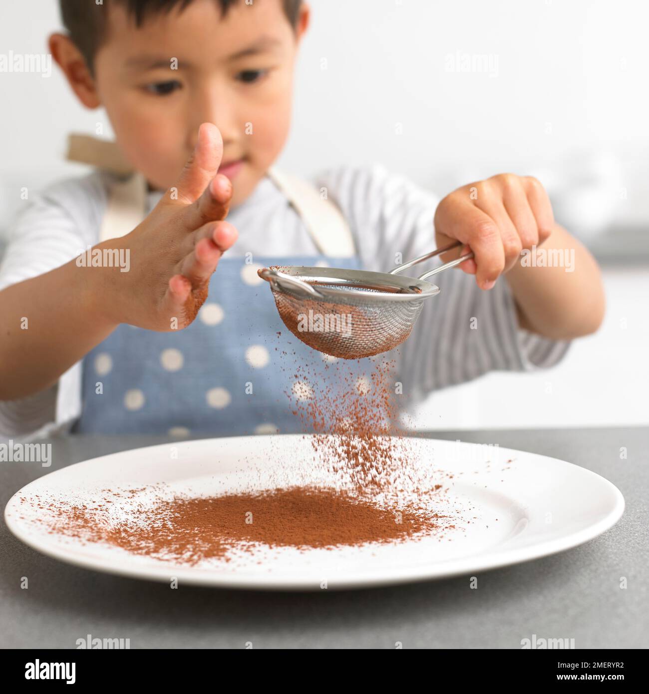 Ragazzo setacciando la polvere di cioccolato su un piatto, 4 anni Foto Stock