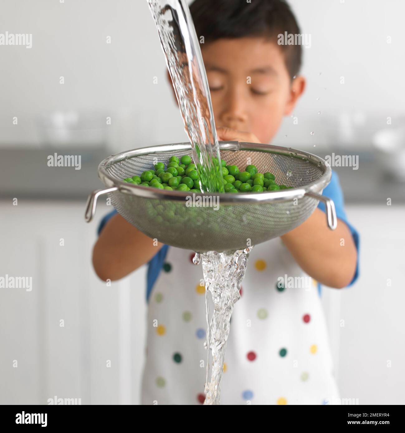 Ragazzo drenante poi rinfrescante con setaccio d'acqua fredda pieno di piselli cotti, 4 anni Foto Stock