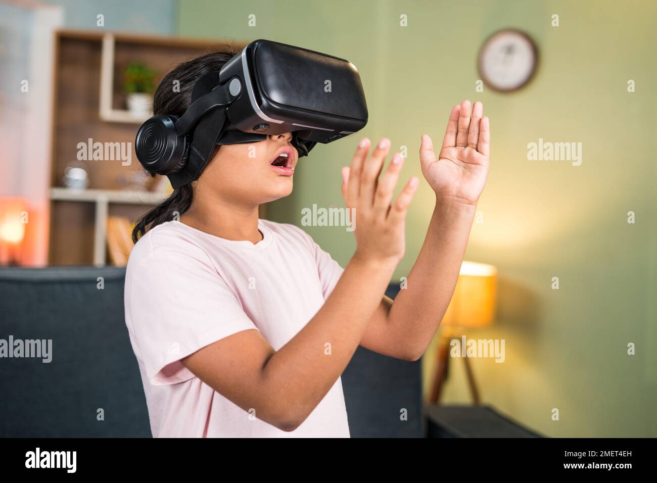 Ragazza eccitata con un'esperienza di wow durante l'uso di realtà virtuale o di visore per realtà virtuale che percepiva oggetti cercando di toccare in aria sul metaverse - concetto di Foto Stock