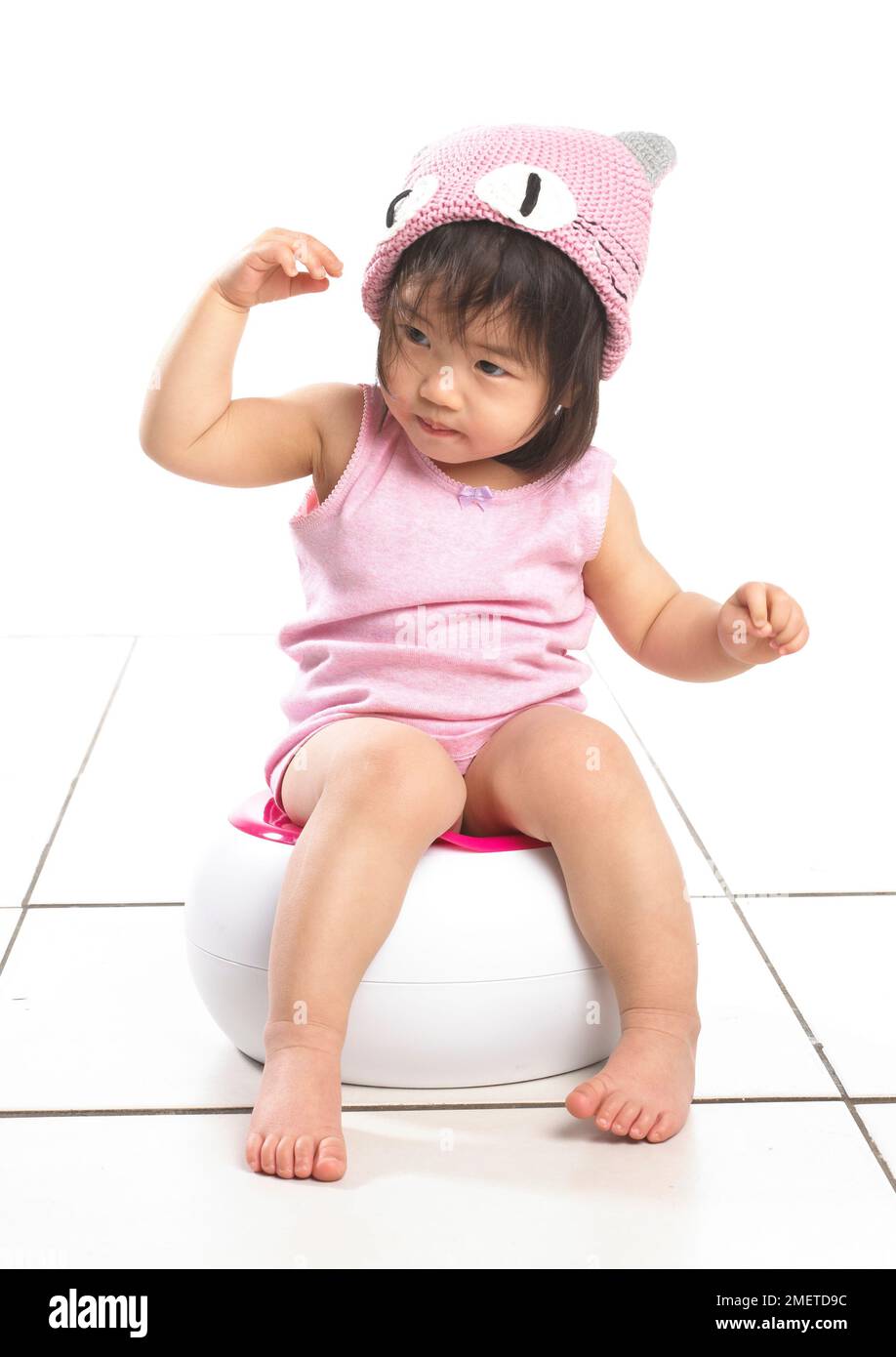 Ragazza che indossa giubbotto rosa seduto su vasino bianco, con cappello di lana rosa, 20 mesi Foto Stock