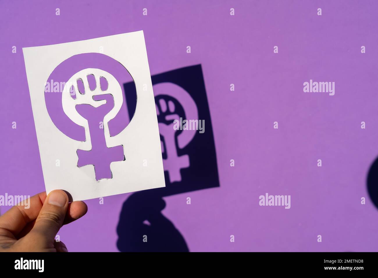 Una donna che detiene il simbolo della lotta per il femminismo su uno sfondo viola, pugno clenched di una donna alle proteste di marcia per i diritti delle donne e. Foto Stock