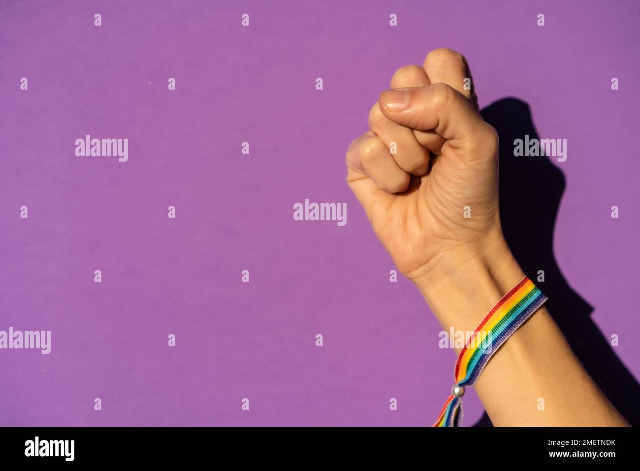 Mano di una donna con pugno chiuso duro sul simbolo di lotta a favore del femminismo, sfondo viola, lotta a favore delle donne, forza femminile, bandiera LGTB Foto Stock