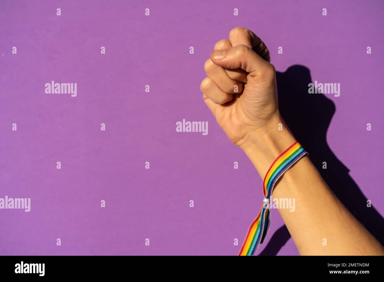 Mano di una donna con pugno chiuso in simbolo femminismo a favore del femminismo, sfondo viola, lotta a favore delle donne, forza femminile, bandiera LGTB Foto Stock