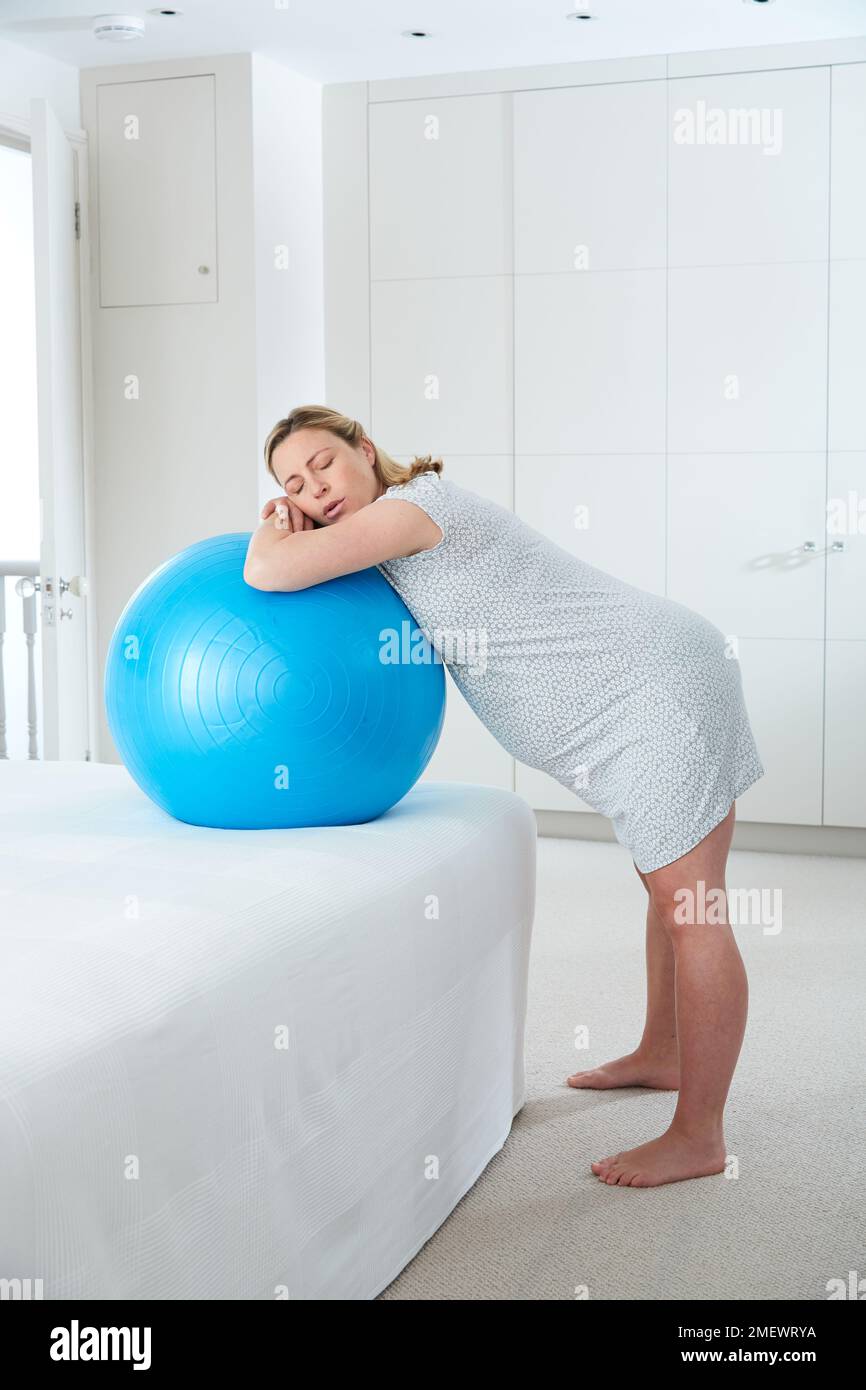 9 mesi / 40 settimane di gravidanza in travaglio a casa. In piedi appoggiati su una palla da parto su un letto, fase attiva del travaglio. Foto Stock