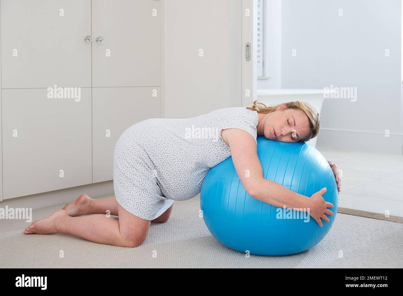 9 mesi / 40 settimane di gravidanza in travaglio a casa. Inginocchiarsi con una palla di birthibg, fase attiva di travaglio. Foto Stock