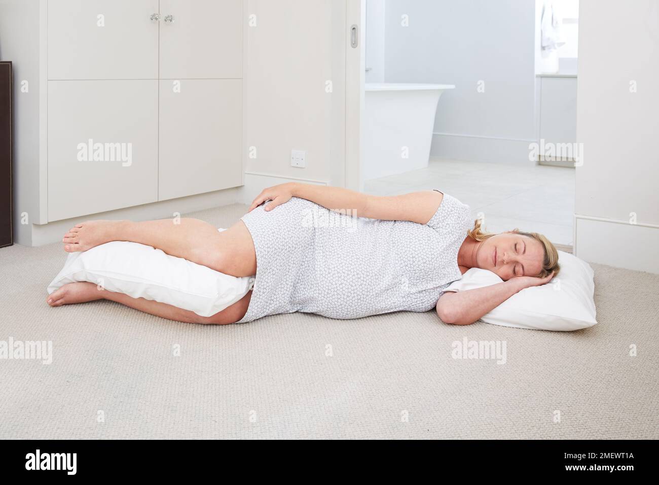 9 mesi / 40 settimane di gravidanza in travaglio a casa. Sdraiata sul fianco del pavimento, con un cuscino tra le ginocchia. Fase di riposo del lavoro. Foto Stock