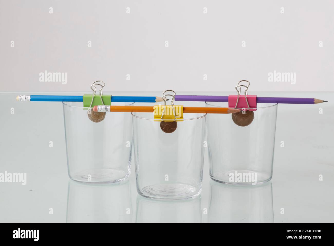 Clip e matita che tengono una moneta in un bicchiere Foto Stock