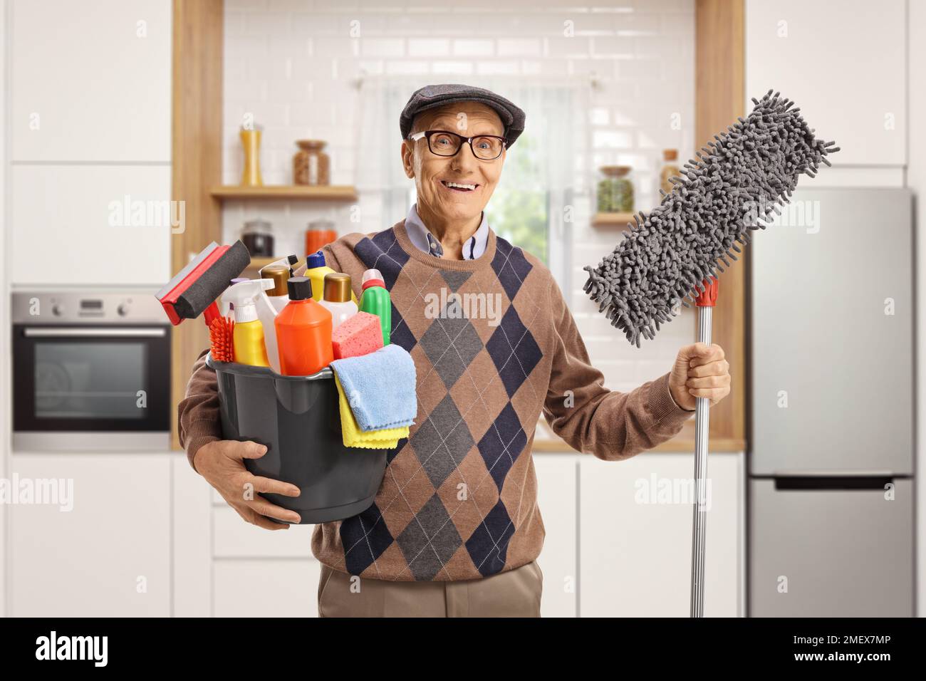 Uomo anziano che tiene un secchio con i rifornimenti di pulizia e un pavimento mop all'interno di una cucina Foto Stock