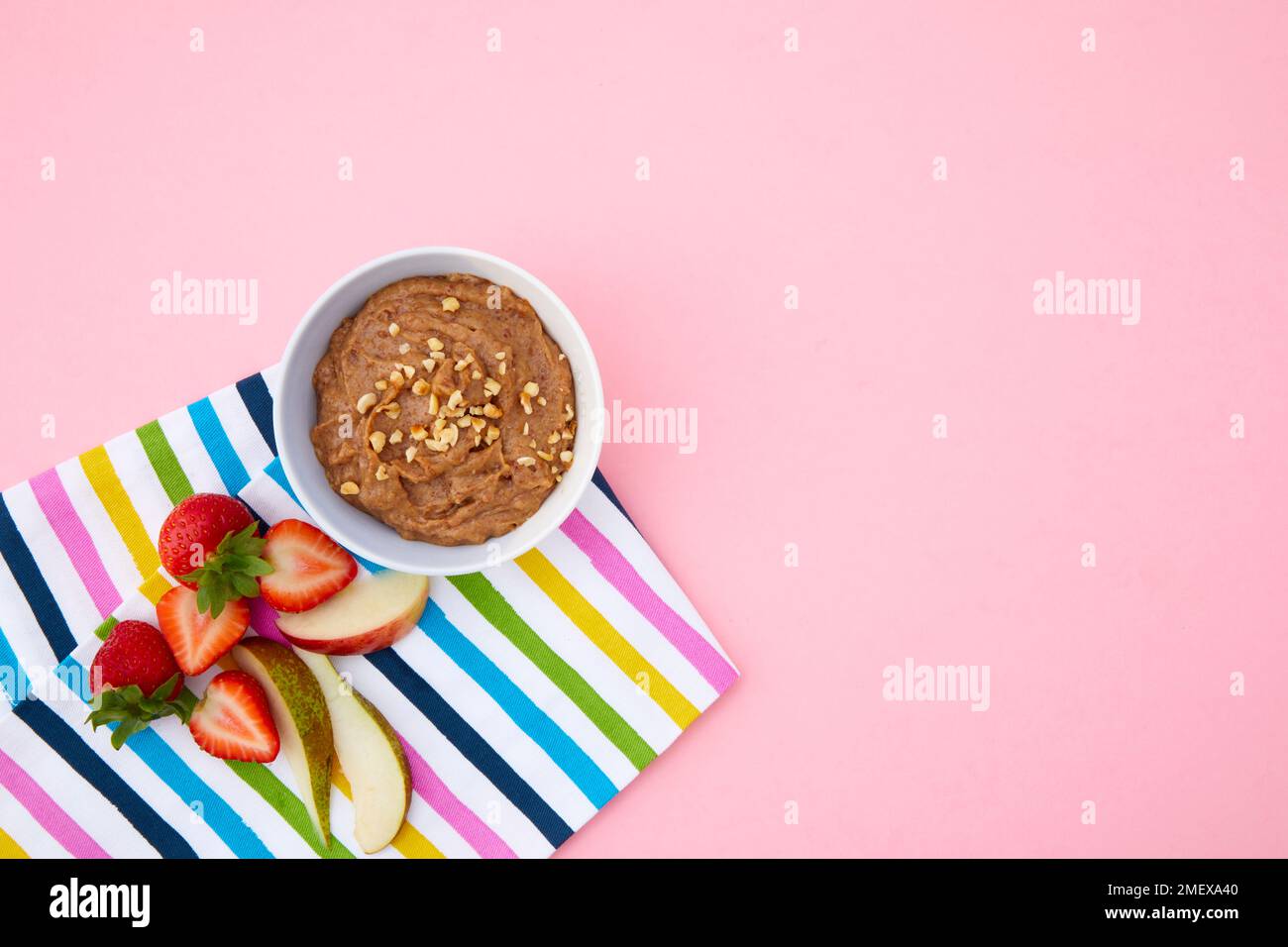 Ciotola di burro di mandorle su fondo rosa con teglia da tè striato e frutta da immergere Foto Stock
