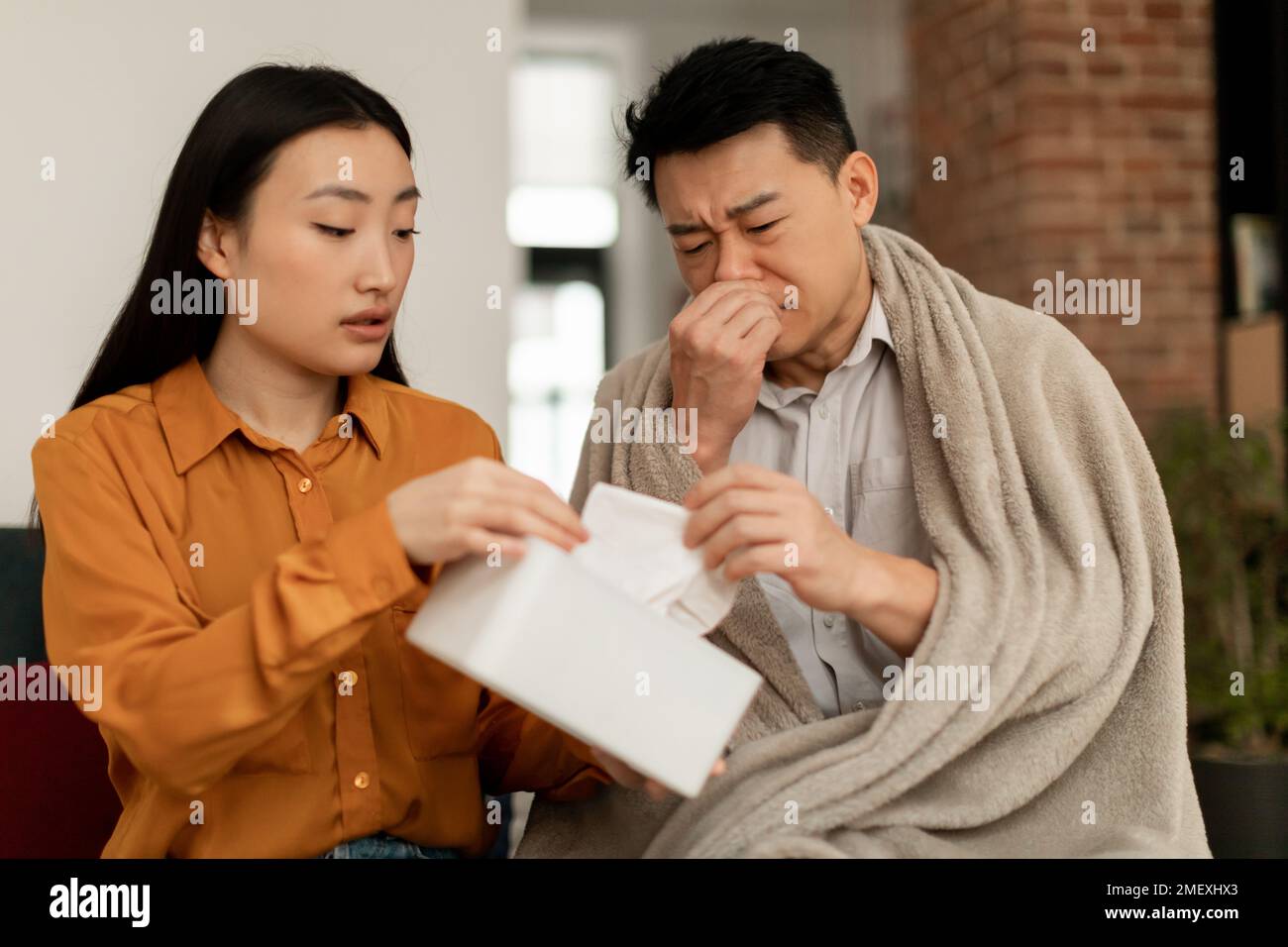 Donna asiatica d'amore che si prende cura di marito malato, moglie che dà nupkins a uomo malato, seduto sul divano a casa Foto Stock