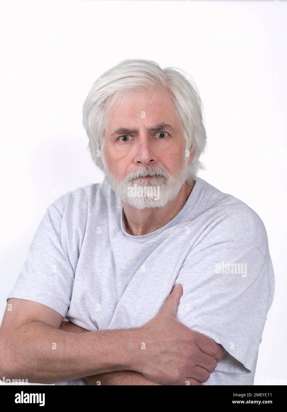 Ripresa verticale di un vecchio uomo dall'aspetto arrabbiato con capelli bianchi su sfondo bianco. In piedi dalla vita in su. Foto Stock
