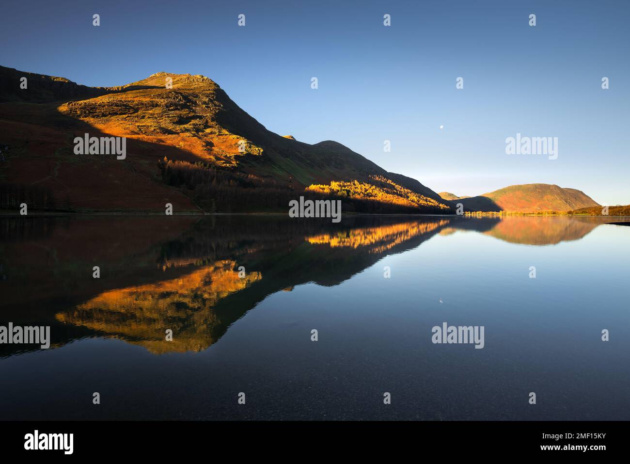 Riflessi a specchio a Buttermere con cielo blu e luce del sole dorata sulle montagne, Lake District, Regno Unito. Foto Stock