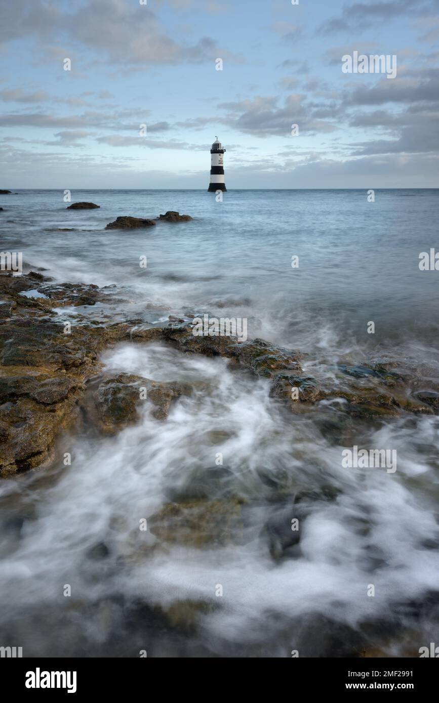 Penmon Point Lighthouse sulla costa di Anglesey, Galles del Nord. Onde che si infrangono in primo piano all'alba. Foto Stock