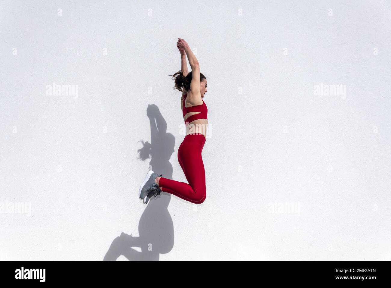 Donna sportiva che salta in aria contro una parete bianca al sole. Foto Stock