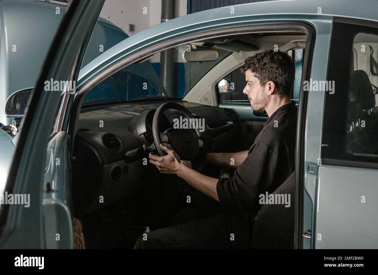 Vista laterale del tecnico maschile seduto in automobile e controllo delle informazioni sulla risoluzione dei problemi durante il lavoro in officina Foto Stock