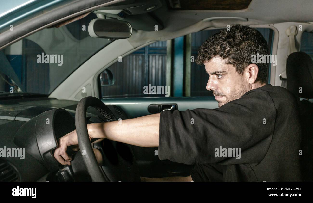 Vista laterale del tecnico maschile seduto in automobile e controllo delle informazioni sulla risoluzione dei problemi durante il lavoro in officina Foto Stock
