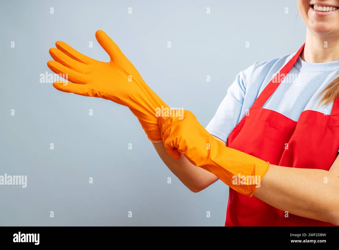 Donna con grembiule rosso che indossa guanti protettivi su sfondo blu Foto Stock