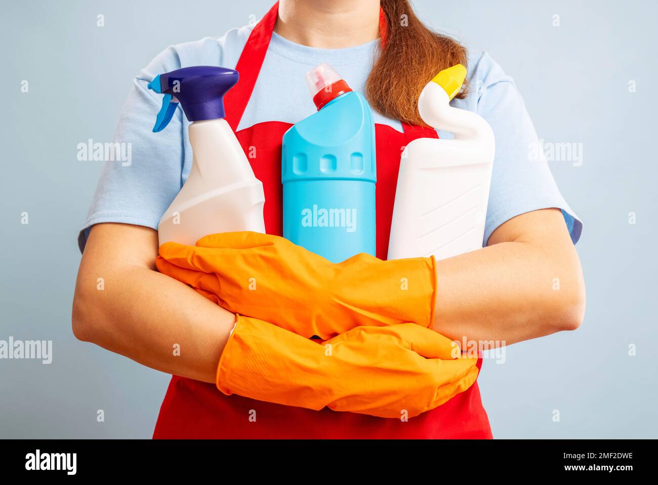 Donna con guanti e grembiule che tiene prodotti detergenti su sfondo blu Foto Stock