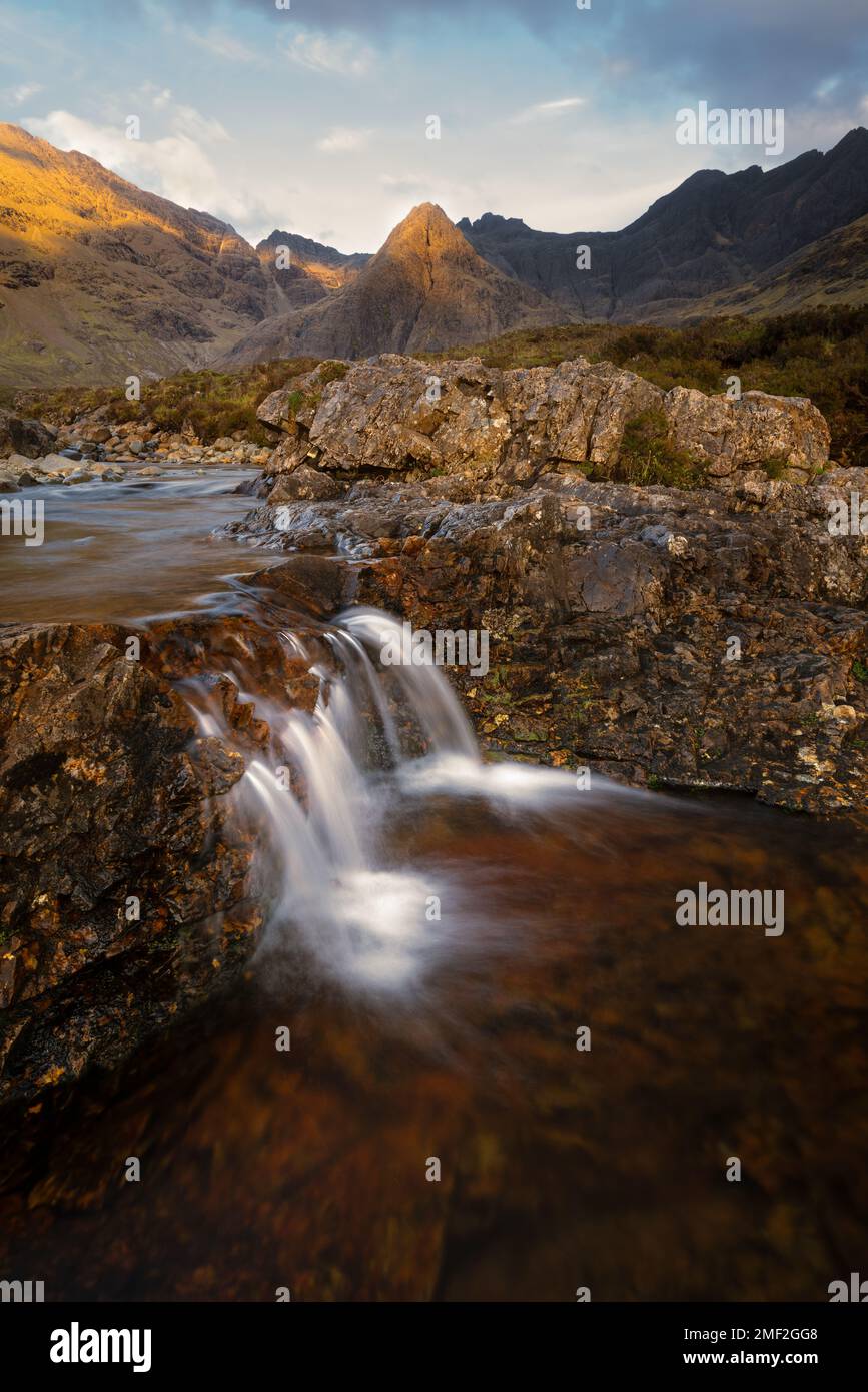 Piccola cascata a gocciolamento con vista mozzafiato delle montagne di Cuillin appese di luce dorata. Fairy Pools, Isola di Skye, Scozia, Regno Unito. Foto Stock