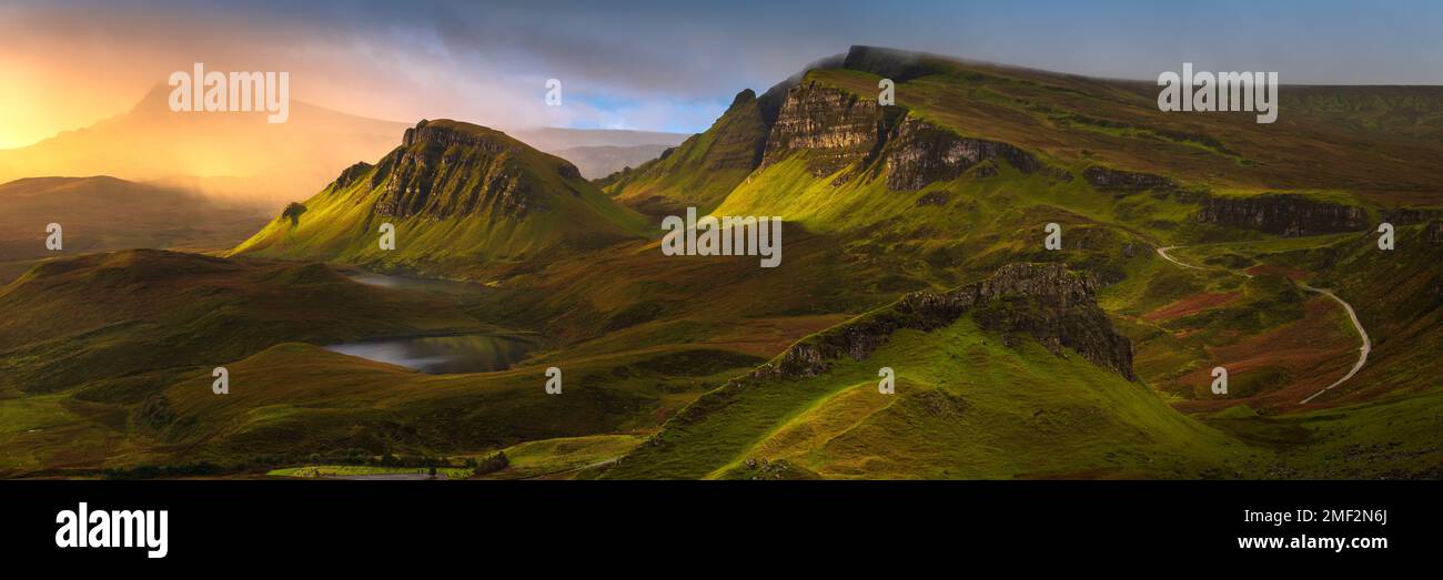 Vista panoramica di Quiraing all'alba sull'isola di Skye, Scozia, Regno Unito. Luce dorata che si infrange attraverso le nuvole di tempesta drammatiche. Foto Stock