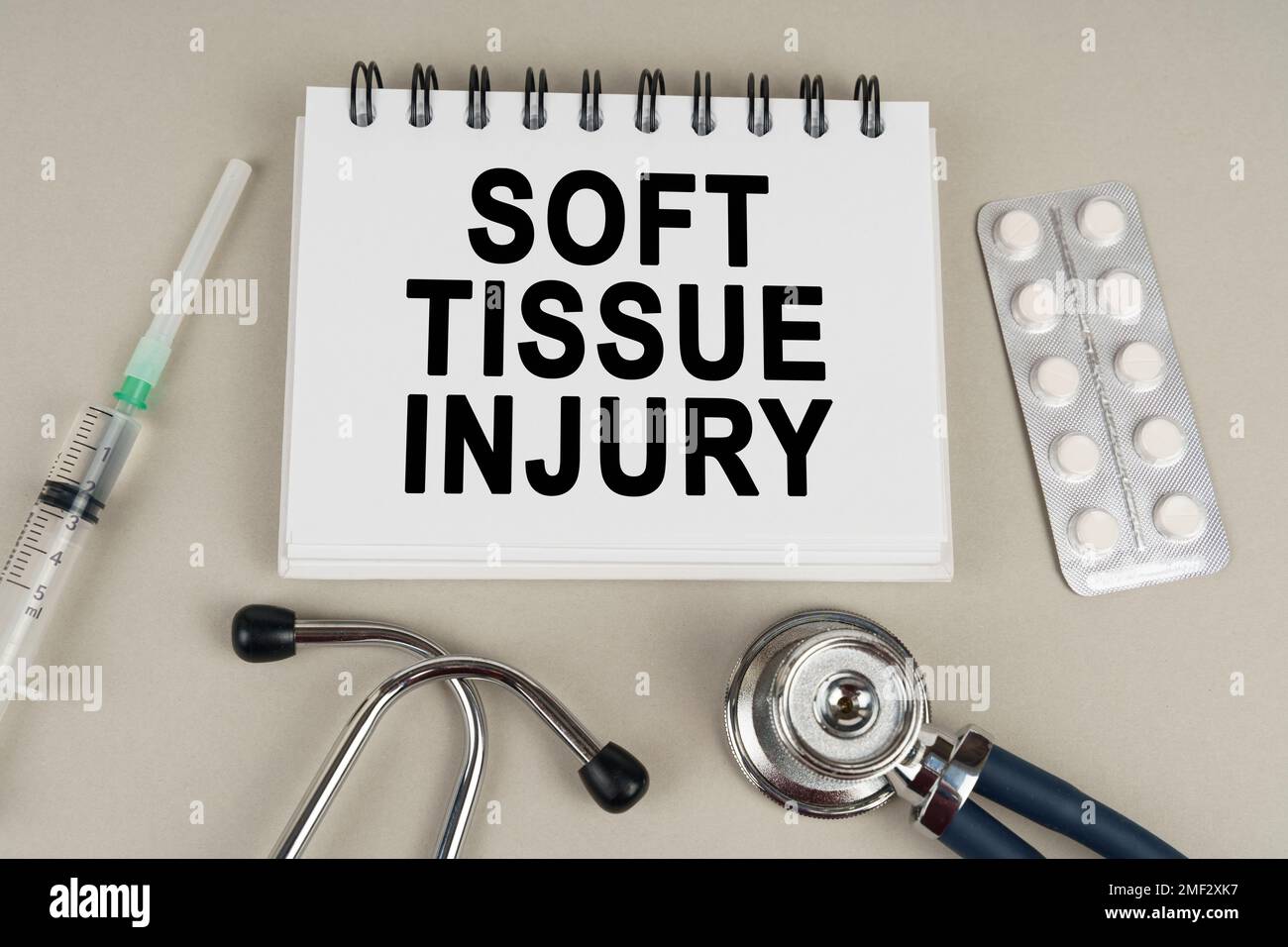Concetto medico. Su una superficie grigia, una siringa, un termometro, uno stetoscopio, un blister e un blocco note con la scritta - lesione del tessuto molle Foto Stock