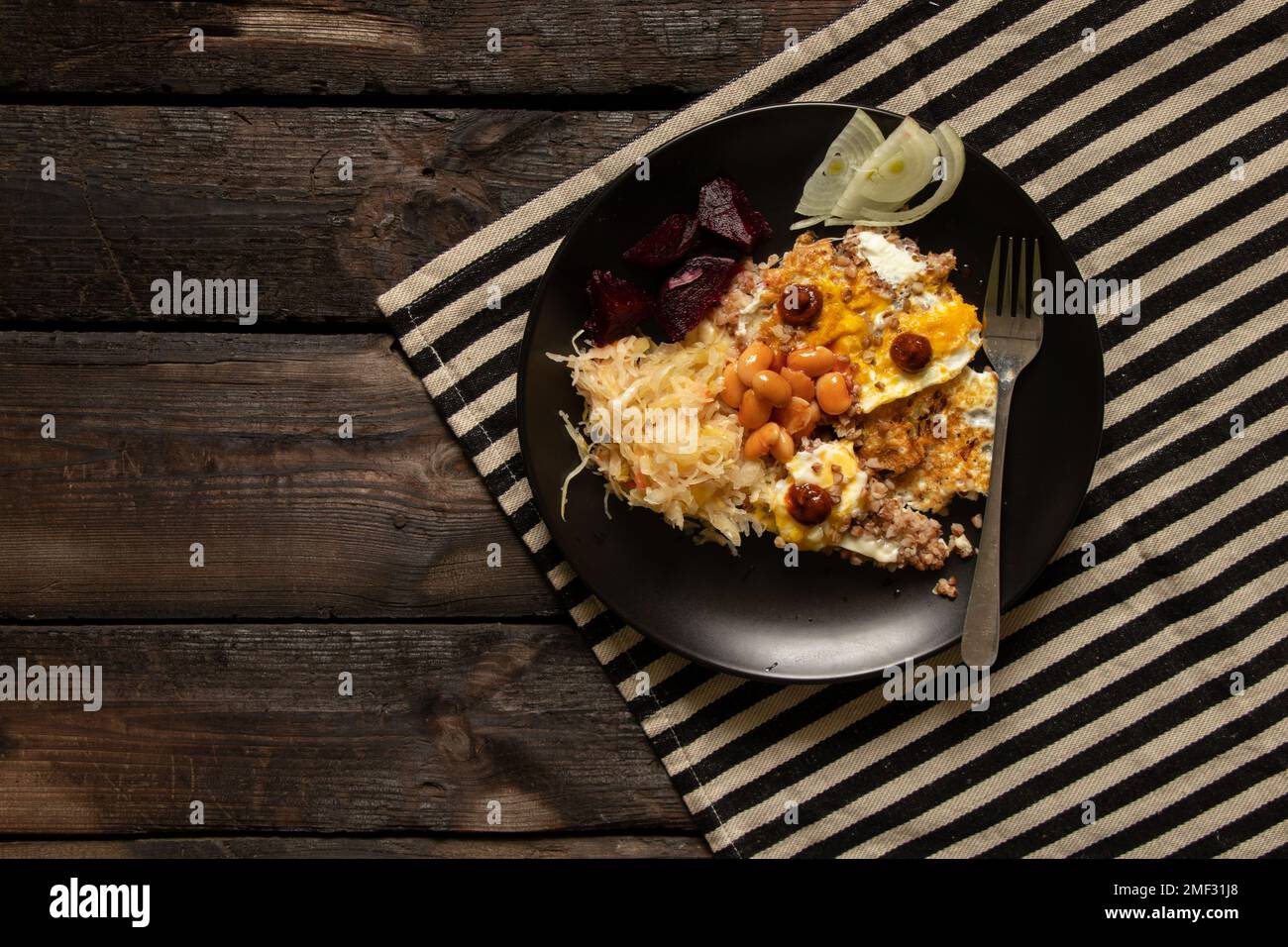 uova strapazzate con verdure in un piatto nero su un vecchio tavolo di legno, pranzo vegano, cibo fatto in casa Foto Stock