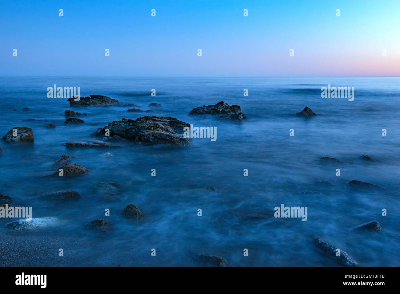 costa, pietre che emergono da acqua ghiacciata, tramonto, colori blu Foto Stock