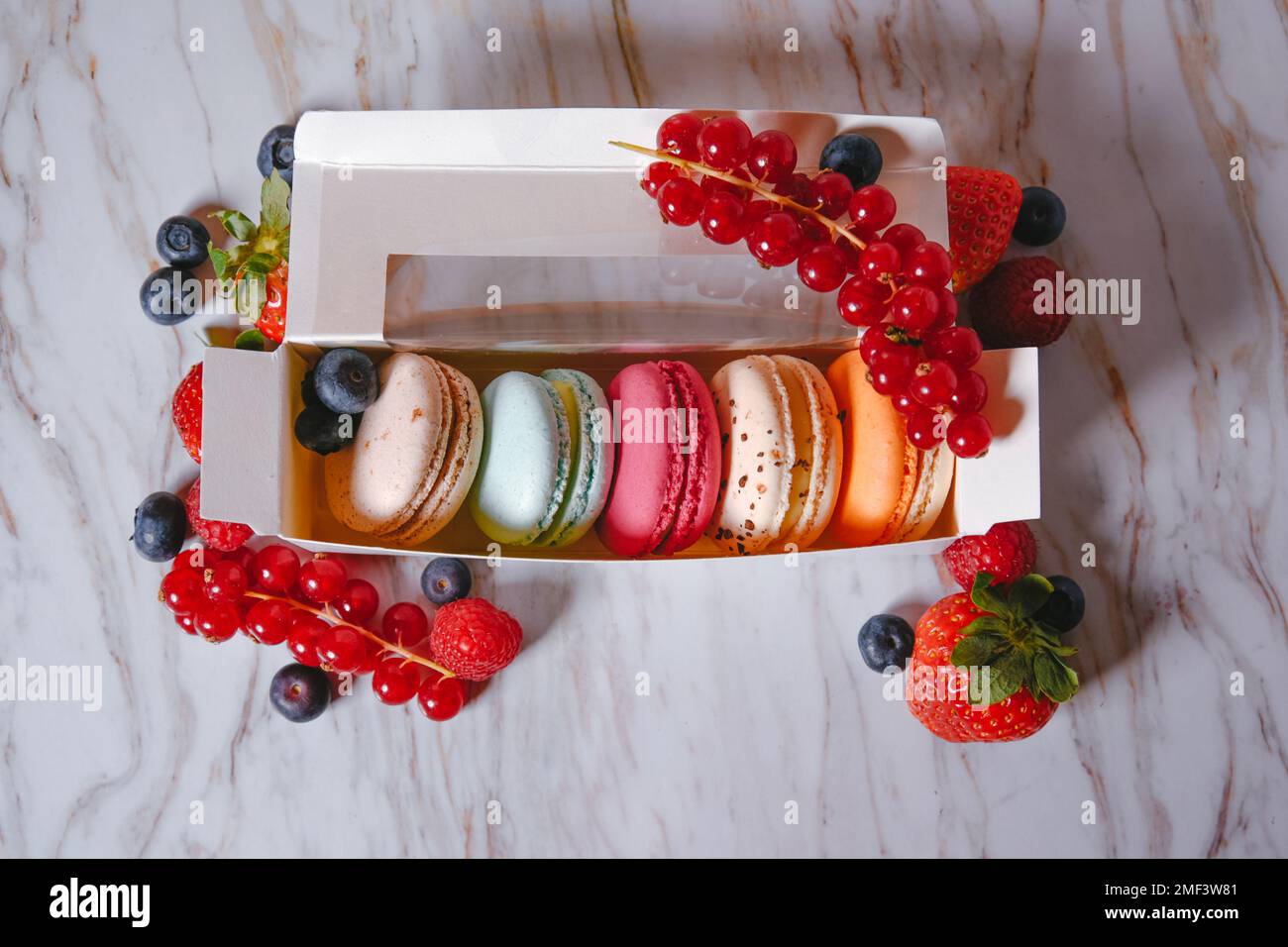 Il dessert di Macaron, una scatola con macaron colorati si trova su uno stile di marmo. Dolci, dieta, regalo per il 8 marzo o 14 febbraio. Fragole e lamponi, b Foto Stock