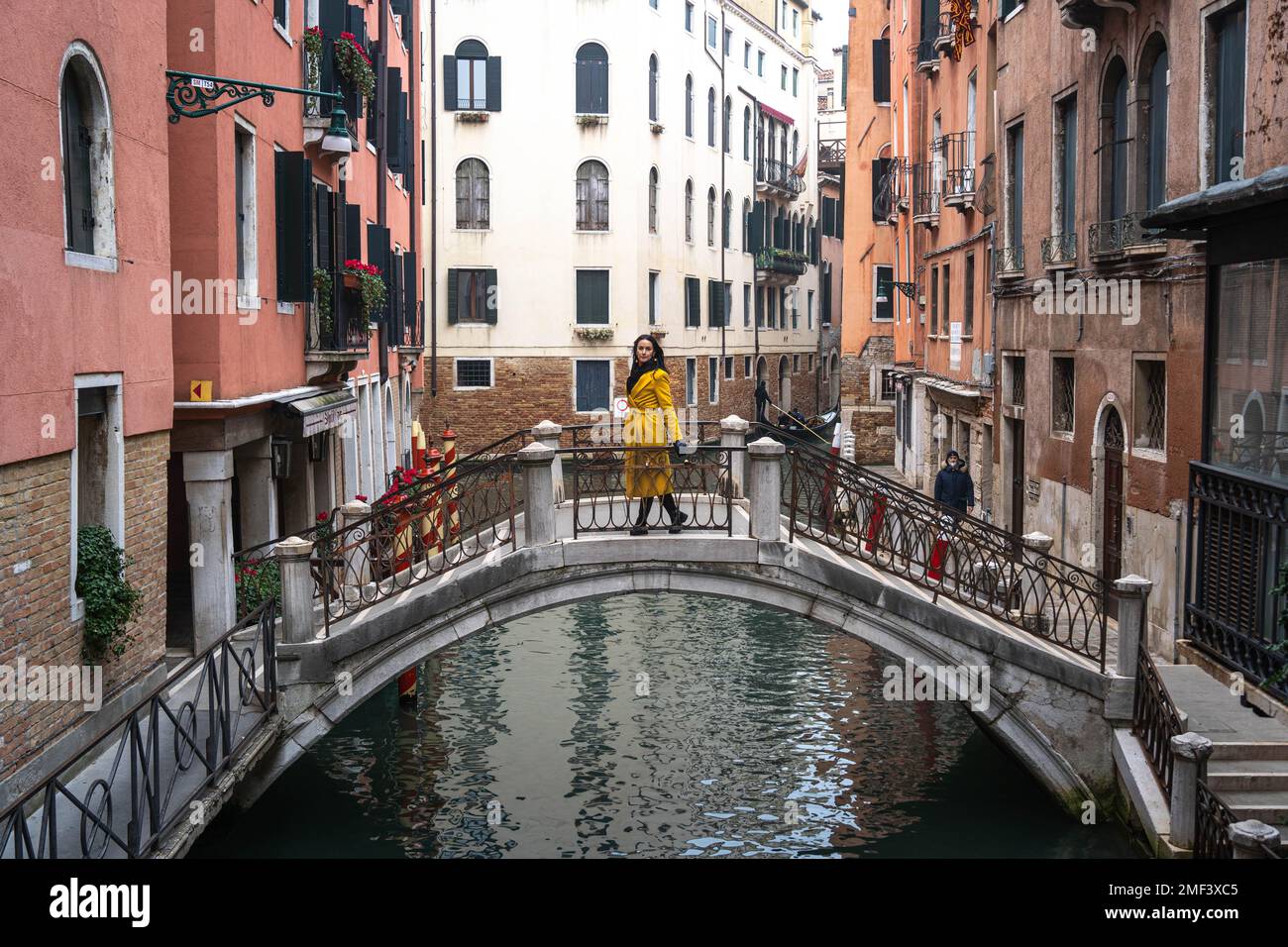 Una donna di colore giallo si erge sola al ponte su un canale di Venezia Foto Stock