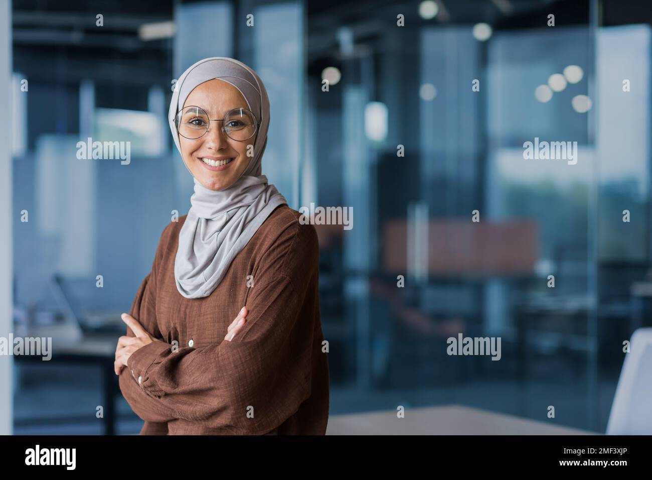 Ritratto di giovane bella donna d'affari araba fiduciosa in hijab. In piedi in ufficio, sorridendo, guardando la telecamera, attraversò le braccia. Foto Stock