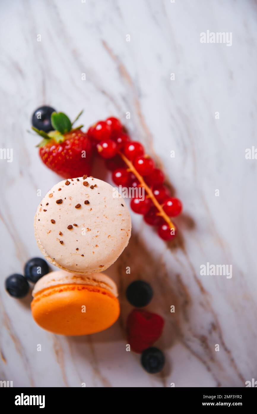 Rosa Macaron, arancione e beige, blu su marmo. Un bellissimo dessert francese. Frutta, fragole e mirtilli, mirtilli, r Foto Stock