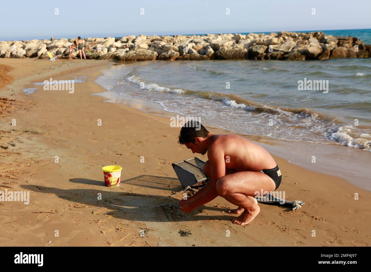 Un uomo che scava per le vongole telline su una spiaggia in Sicilia Foto Stock