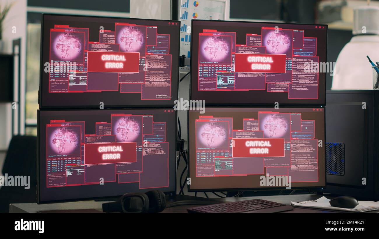 L'ufficio IT visualizza un messaggio di errore critico lampeggiante sullo schermo, più monitor mostrano un avviso di violazione della sicurezza e un arresto anomalo del sistema. Avviso di attacco hacking e malfunzionamento del computer. Foto Stock