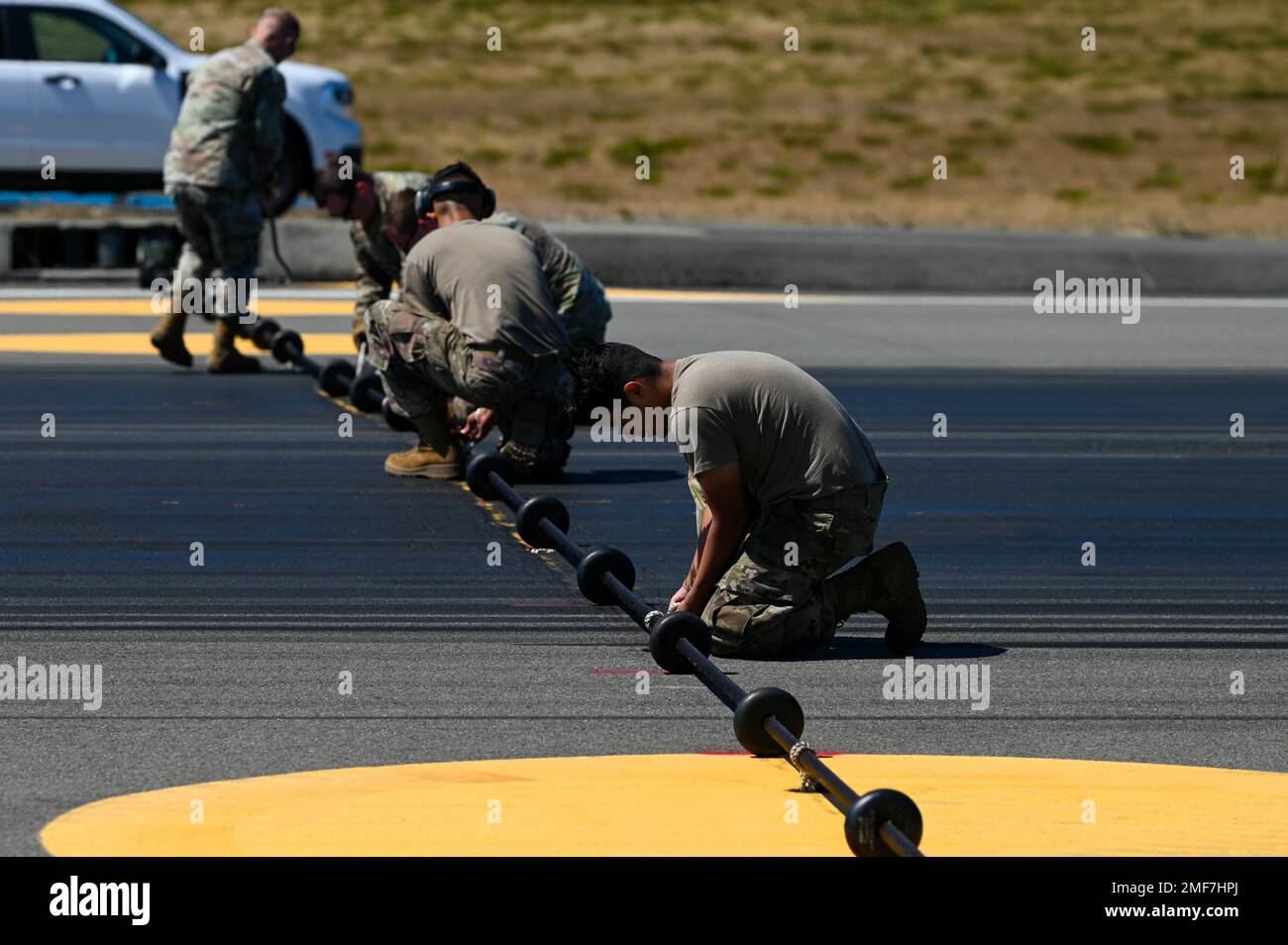 STATI UNITI Air Force Airmen con il 627th Civil Engineer Squadron Tie pendenti funi di fissaggio cavo e verificare la distanza del disco di supporto cavo sulla linea di volo McChord campo alla base Joint Lewis-McChord, Washington, 17 agosto 2022. Il sistema di arresto della barriera dell'aeromobile, BAK-12, mantiene la tensione su un cavo massiccio esteso lungo la pista che può catturare l'aeromobile, dotato di un gancio di coda, del peso massimo di 80.000 kg. Foto Stock