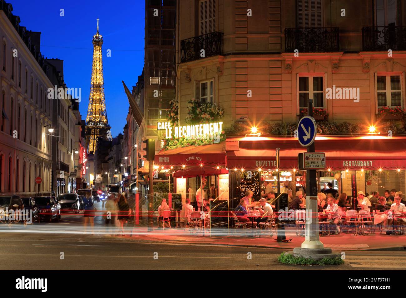 Vista notturna della Torre Eiffel e del Cafe le Recrutement, all'angolo tra Rue Saint-Dominique e Boulevard de la Tour-Maubourg, con veicoli al semaforo posteriore trails.Paris.France Foto Stock