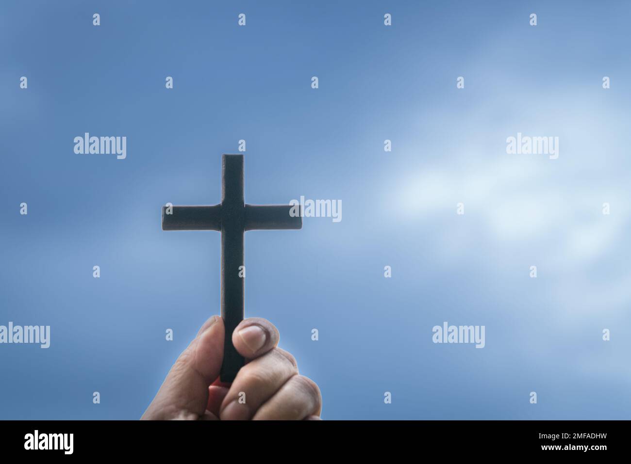 Mano che tiene una croce di legno con cielo nuvoloso blu sullo sfondo. Concetto per la fede cristiana e il Venerdì Santo. Foto Stock