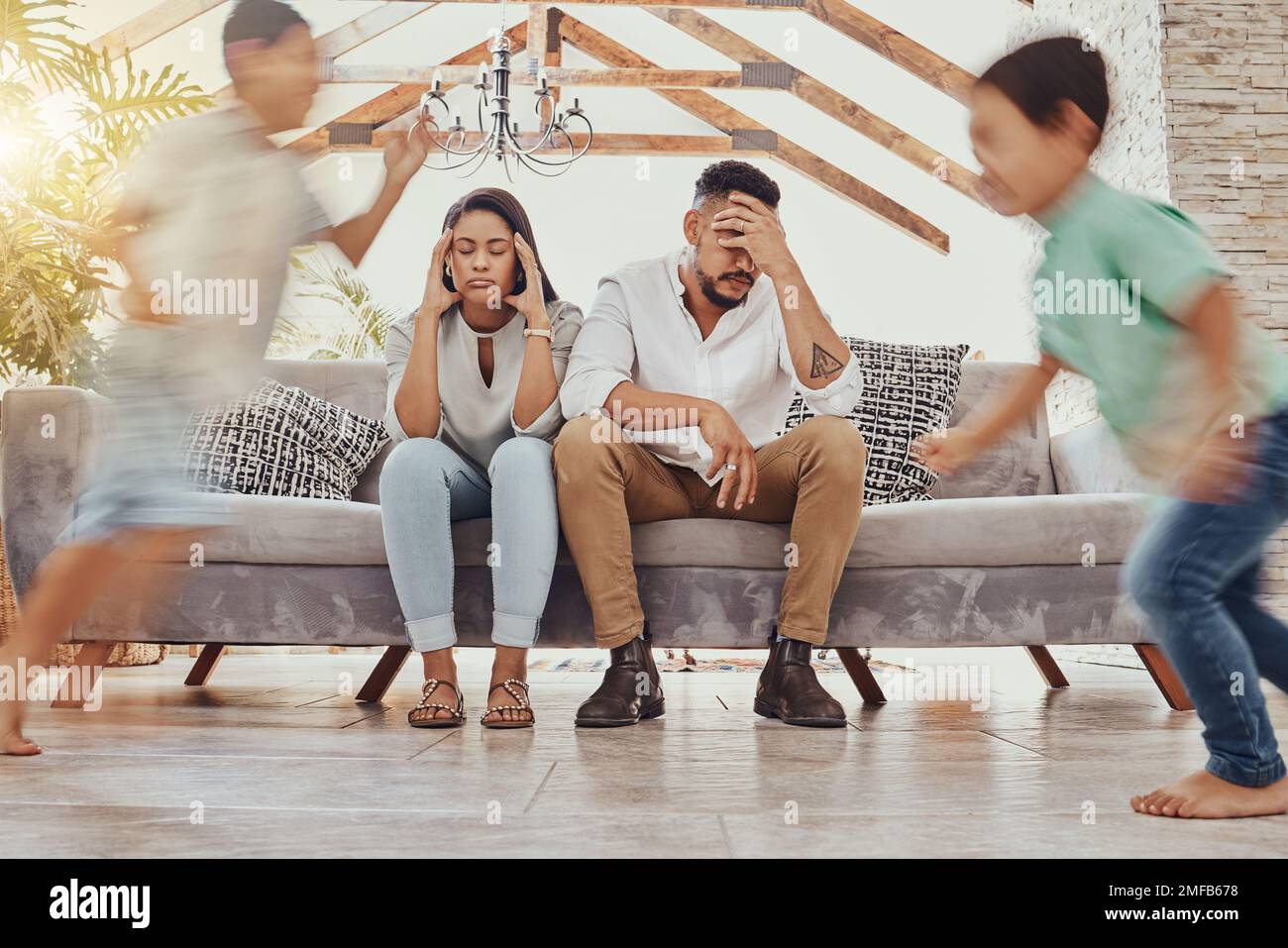 I genitori stanchi, i bambini che corrono e la famiglia in un salotto che sentono ansia, mal di testa e stress. Bambini caos, corsa e fatica di mamma e padre Foto Stock