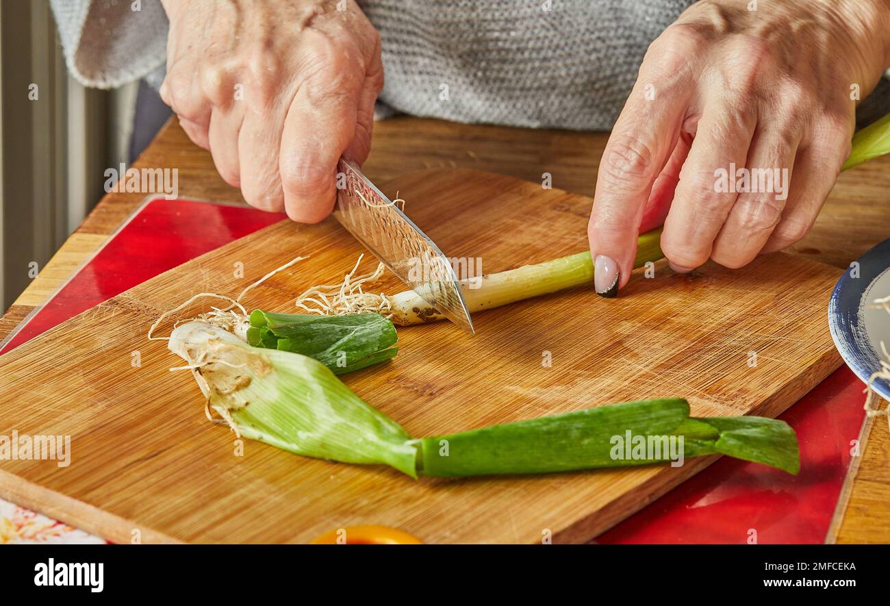 Lo chef taglia il porro in cerchi, in cucina su asse di legno Foto Stock