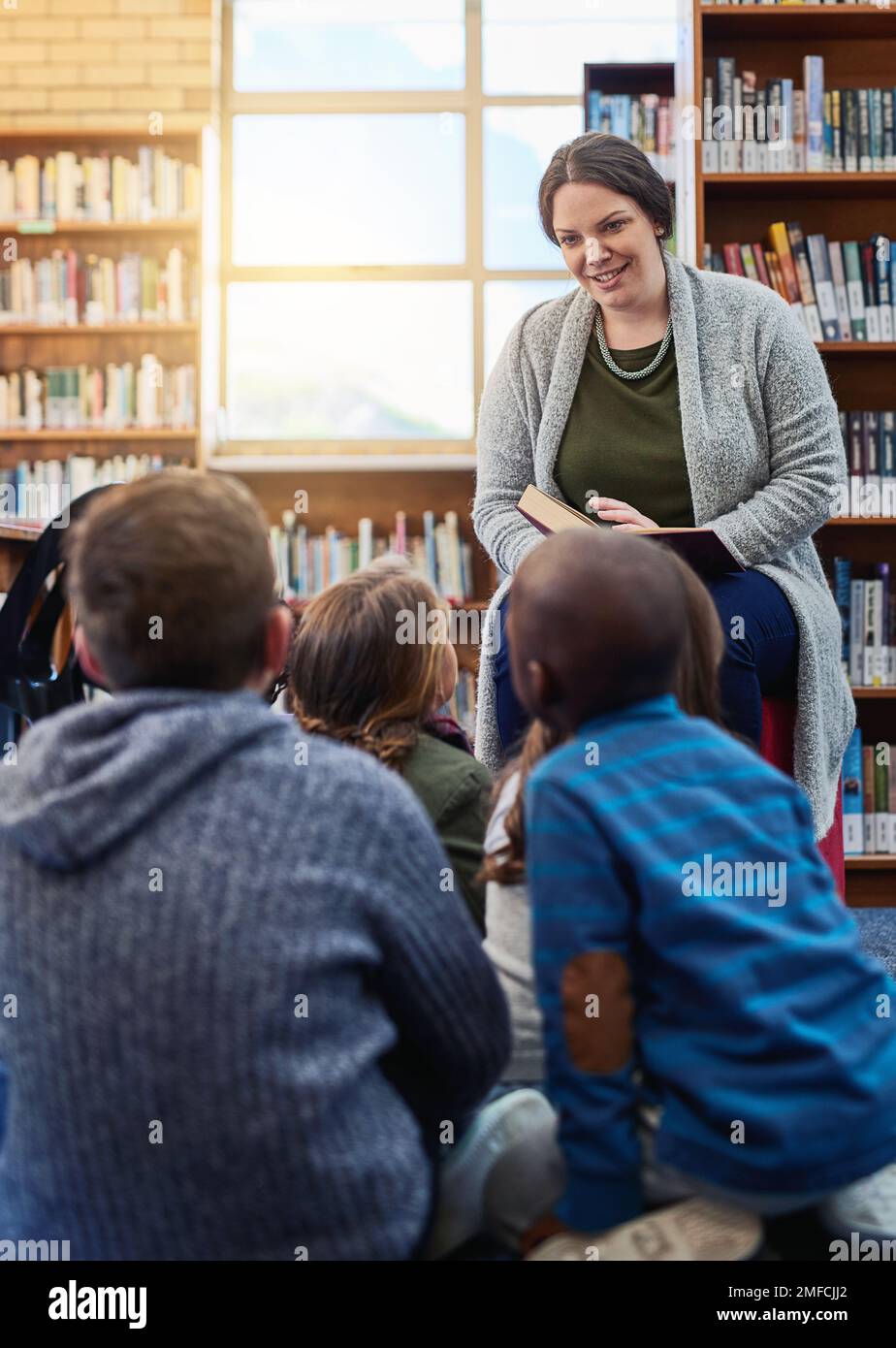 La sua storia a scuola. un insegnante che legge ad un gruppo di ragazzi della scuola elementare in biblioteca. Foto Stock